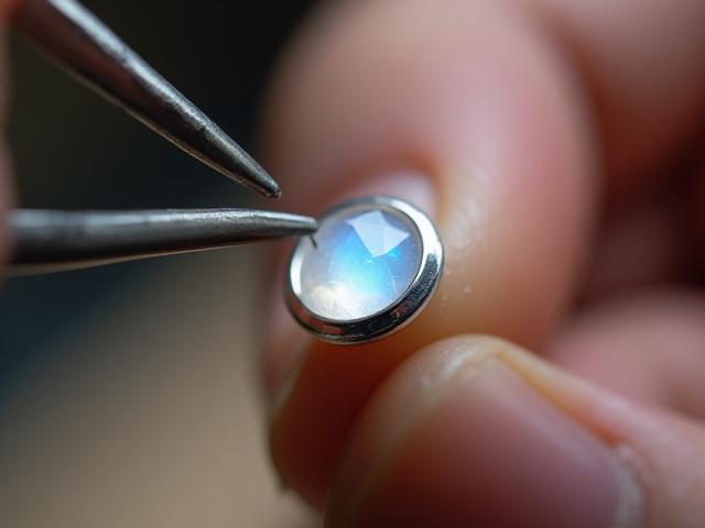 Silversmith carefully placing a gemstone into a sterling silver bezel with tweezers